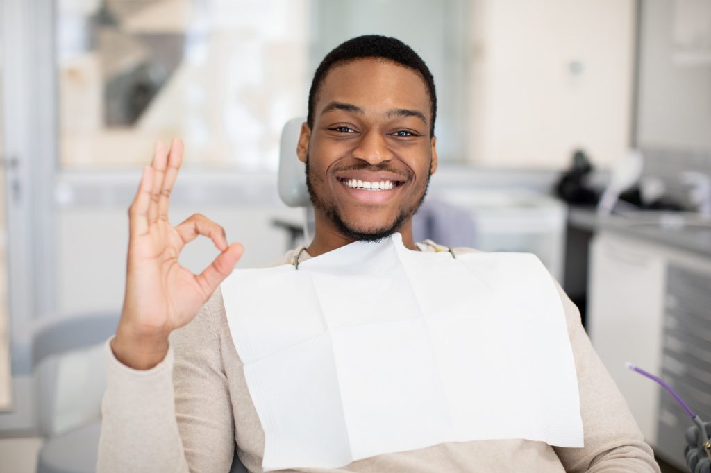 happy male patient sitting in dentist chair and showing ok sign because of gum disease treatment and now better Oral Health